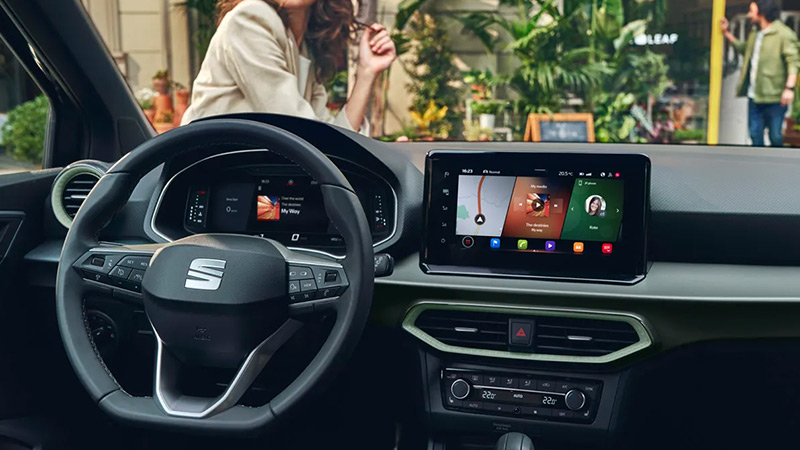Pohled přes přístrojovou desku ven z vozu SEAT Arona před kterým prochází žena 