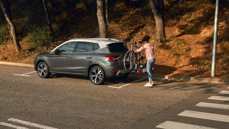 SEAT Arona zaparkovaný u lesa, žena dává kolo na nosič kol 
