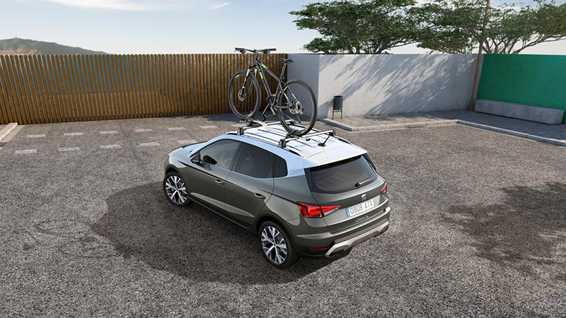 zaparkovaný vůz SEAT Arona nosnými tyčemi na střeše s upevněným kolem