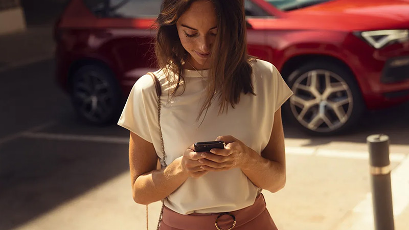 Žena se spojuje přes mobil s vozem SEAT Ateca, který stojí zaparkovaný za ní