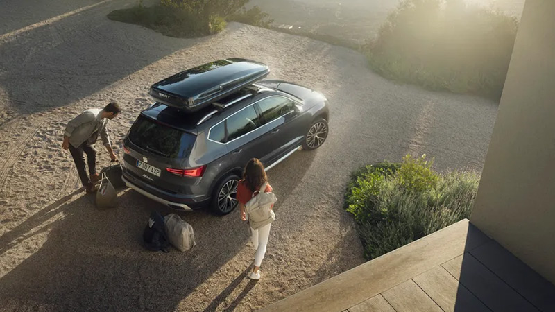 Muž se ženou nakládají zavazadla do šedého SEAT Ateca se střešním boxem