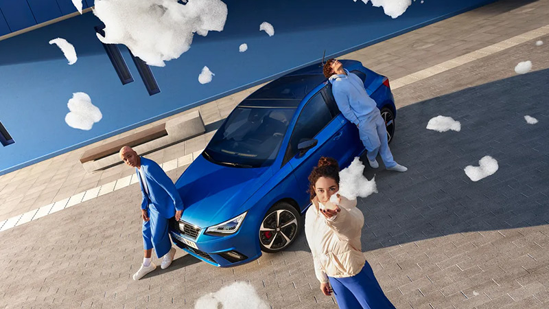 Modrý SEAT Ibiza zaparkovaný u modrého domu, pohled ze předu se 3 pózujícími modely
