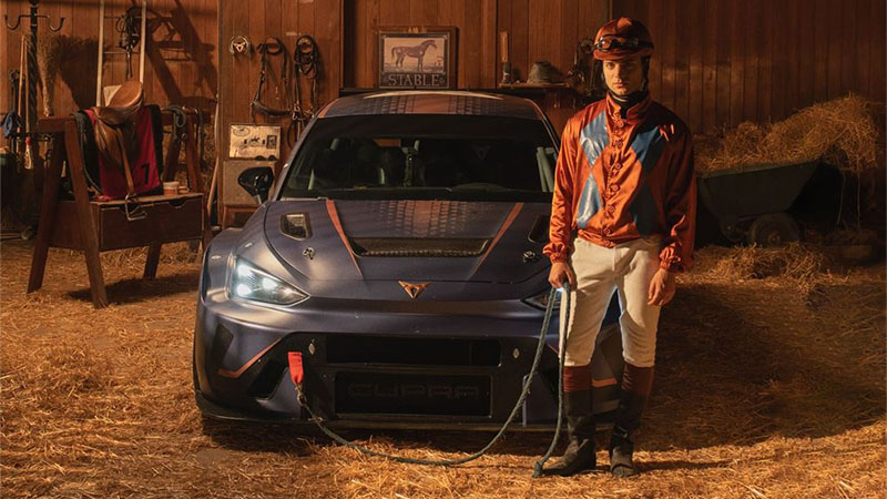 Dostihový jezdec ve stáji stojí vedle sportovního vozu CUPRA.