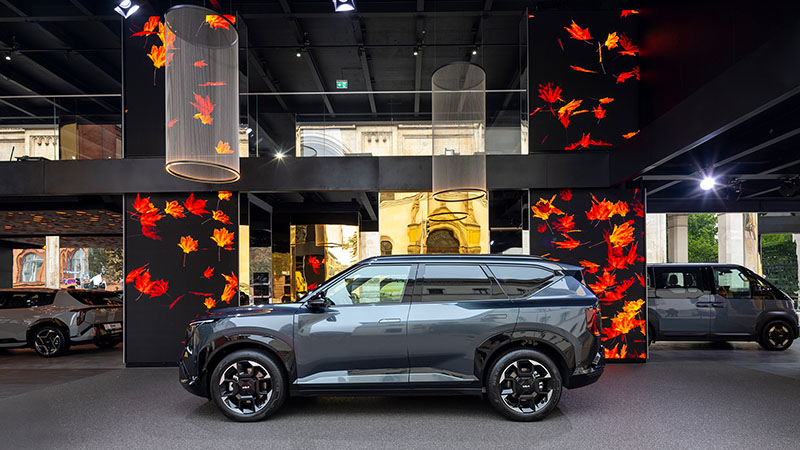 Šedé elektrické SUV Kia EV5 v moderním showroomu s digitální podzimní dekorací.