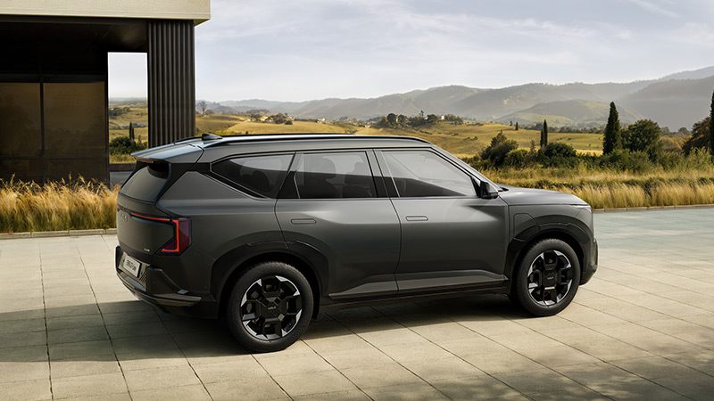 Šedý model Kia EV5 GT Line zaparkovaný před domem v přírodě - pohled z pravého boku