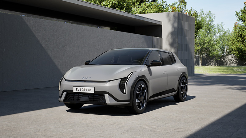 Přední pohled na šedý elektrický vůz Kia EV4 GT-Line zaparkovaný před moderní budovou