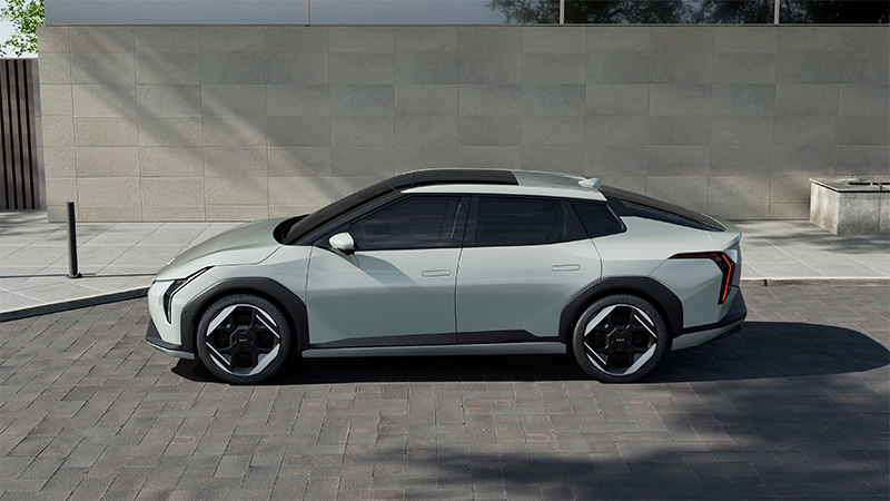 Boční pohled na šedý elektrický vůz Kia EV4 GT-Line zaparkovaný u moderní budovy