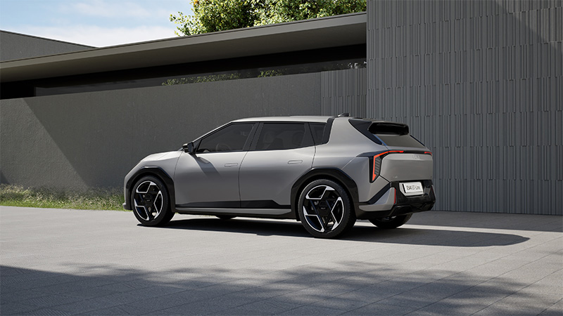 Zadní a boční pohled na šedý elektrický vůz Kia EV4 GT-Line zaparkovaný před moderní budovou