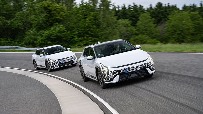 Dva bílé maskované modely elektromobilu Kia EV4 projíždějí zatáčkou na testovací dráze.