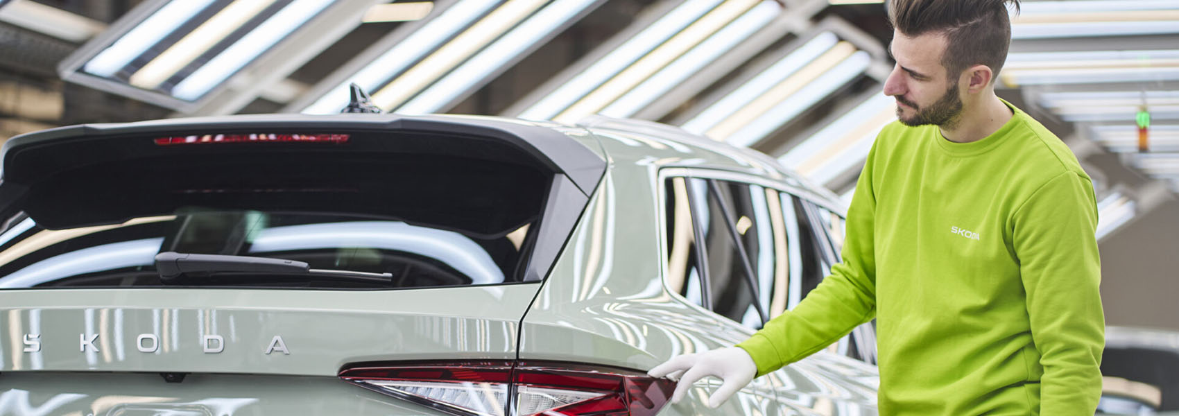 Pracovník Škoda v zářivě zelené uniformě kontroluje zadní světlo SUV na lince