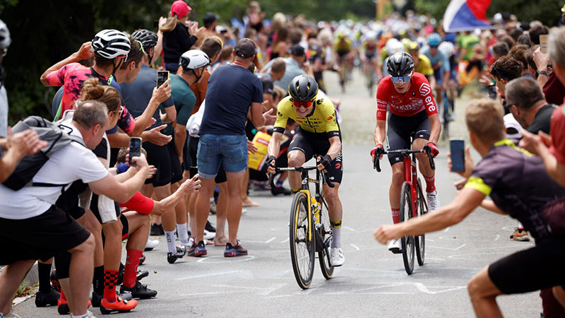 Cyklisté v závodě Czech Tour 2025 projíždějí mezi fanoušky, kteří stojí podél trati